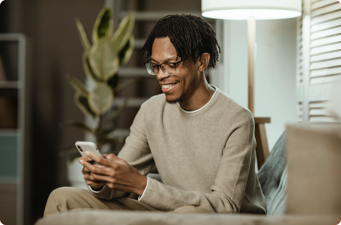 Homem sentado, sorrindo e mexendo no celular
